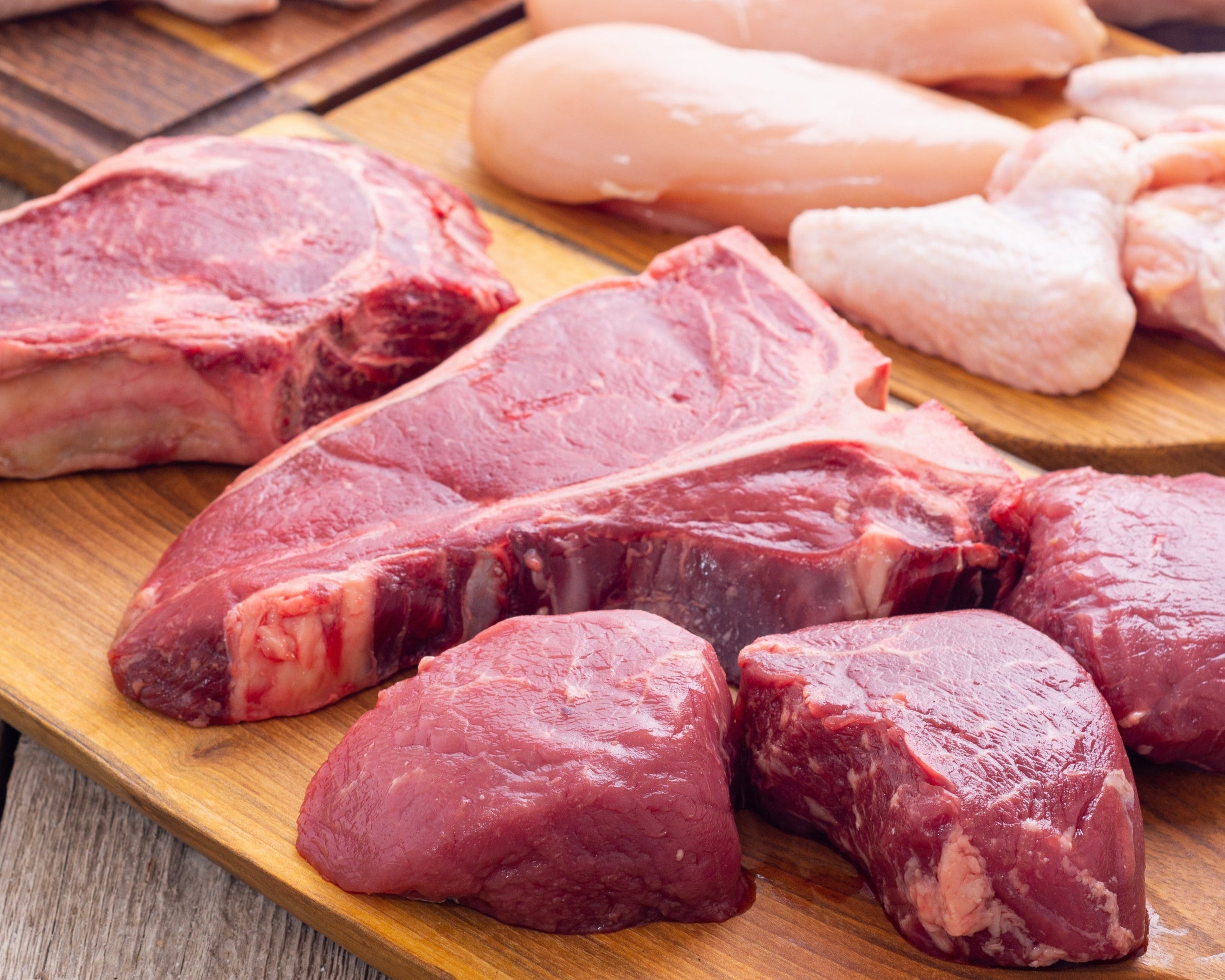 Raw meat and chicken pieces on wooden cutting boards.